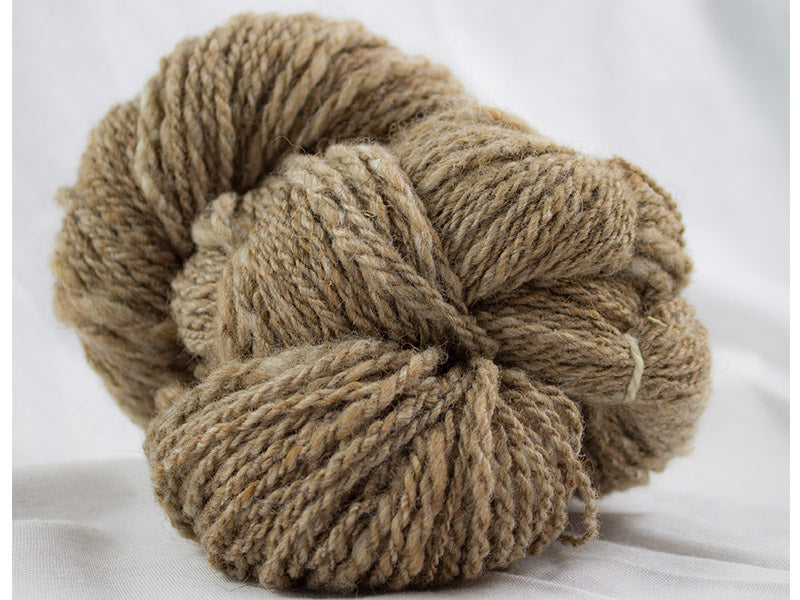 A skein of Burl, a yarn produced by Gothfarm Yarn and made from Shetland wool and alpaca fleece. The yarn is bulky and a dark fawn in color.